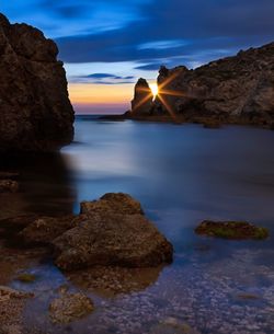 Rocks in sea against sky during sunset