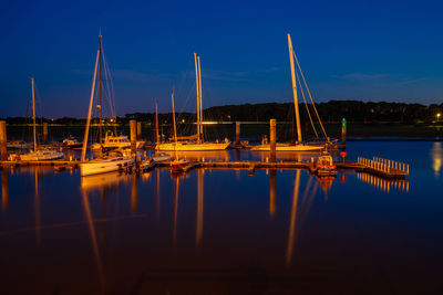 Sailboats moored in harbor against blue sky