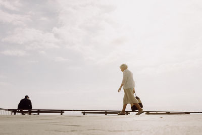 Side view of woman walking on footpath against sky during sunny day