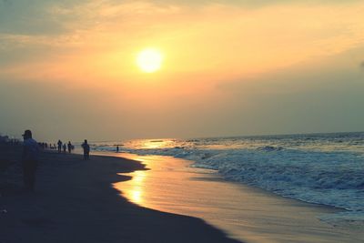 People on beach against sky during sunset