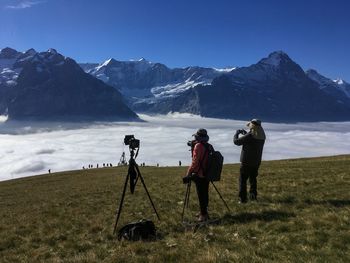 Man and woman photographing snowcapped mountains amidst cloudscape