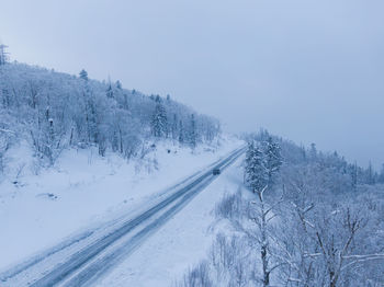 Snow covered road by trees against sky