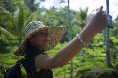 Teen girl wearing a big straw hat taking selfies using mobile phone