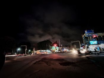 Cars on road by illuminated buildings against sky at night