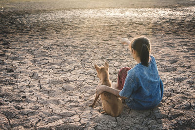 High angle view of girl with dog sitting on field during drought