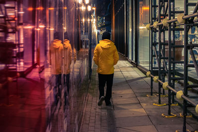 Rear view of woman walking on illuminated footpath amidst buildings at night