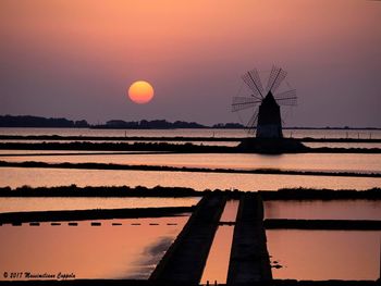 Silhouette traditional windmill by sea against orange sky