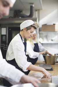 Side view of female baker baking with colleagues in commercial kitchen
