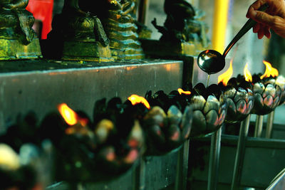 Cropped hand pouring oil in burning diyas at buddhist temple