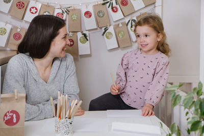 Mother with toddler child writing christmas letter and doing advent calendar tasks in kids room