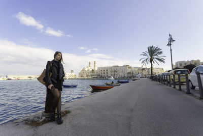 Woman standing on shore against sky in city