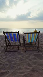 Deck chairs on beach against sky