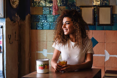 Smiling young woman holding drink while looking away in cafe