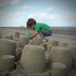 Side view of boy playing with sand on sea shore