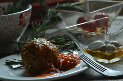 Meatballs and red sauce on plate, fork, green olives in glass dish