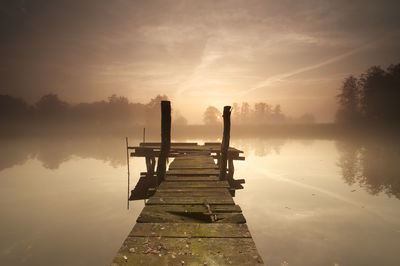 Pier on lake against sky during sunset