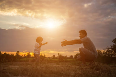 Father and son on field against sky during sunset