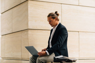 Young man using mobile phone while sitting on wall