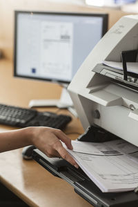 Cropped hand holding paper in printer on table in office