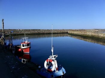 Boats moored in lake against clear blue sky