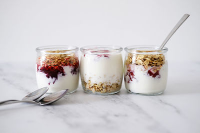 Three jars of oat granola with greek yogurt and nuts on a light background