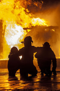 Rear view of silhouette firefighters crouching against fire at night