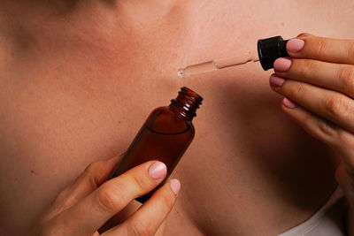 Woman holds brown bottle with cosmetic oil in hands against her body, natural skin care products