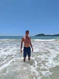 Portrait of shirtless man standing on beach against clear sky