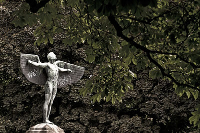 Winged statue against lush trees