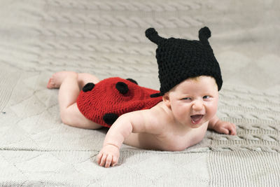 Smiling baby wearing knitted ladybug costume while lying on bed