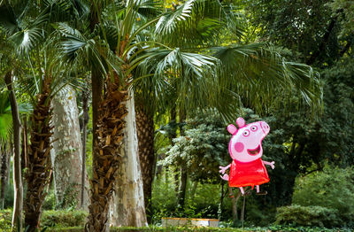 A cheerful red piggy balloon contrasts amidst the surroundings of exotic  plants, low perspective