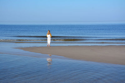 Rear view of girl walking on shore at beach against sky during sunny day
