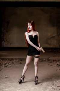 Full length of sensuous woman with handgun standing against wall