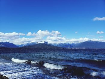 Scenic view of sea by mountains against blue sky