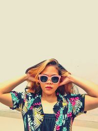 Portrait of young woman wearing sunglasses standing against wall