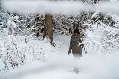 Rear view of woman walking amidst trees during winter