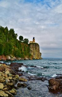 Lighthouse on rocks by sea against sky