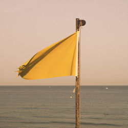 Yellow flag on pole by sea against clear sky