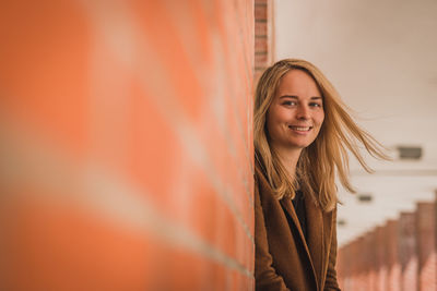 Portrait of smiling beautiful woman with blond hair standing by architectural column