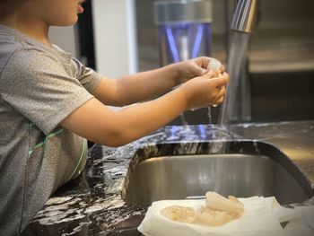 Midsection of boy cleaning food at sink