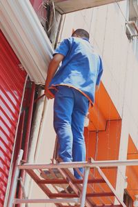 Rear view of man working on a ladder performing paint job