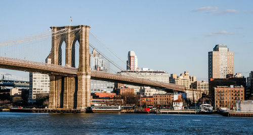 Bridge over river by buildings against sky