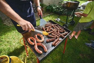 High angle view of men preparing sausages on barbecue grill in yard