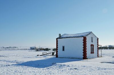 Windmill on snow covered field against clear blue sky