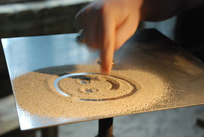 Cropped image of hand making smiley face with sand on table