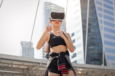 Young woman using virtual reality simulator standing against building in city