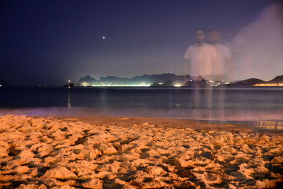 Digital composite image of man standing at beach against sky at night