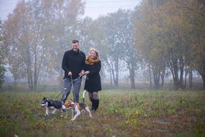 A young happy family couple with two dogs walks in the autumn park in misty morning