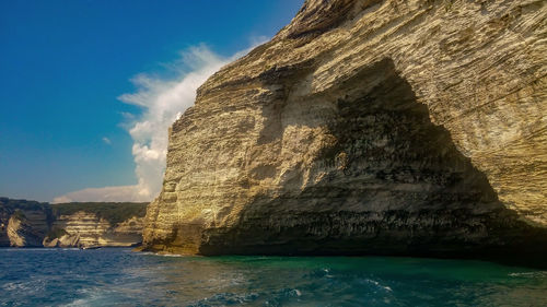 Rock formations and sea caves by sea against sky