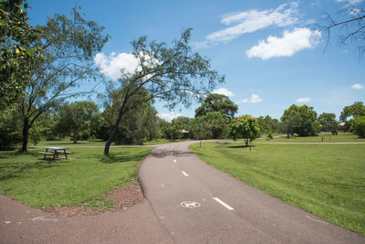 Empty road amidst trees on field against sky